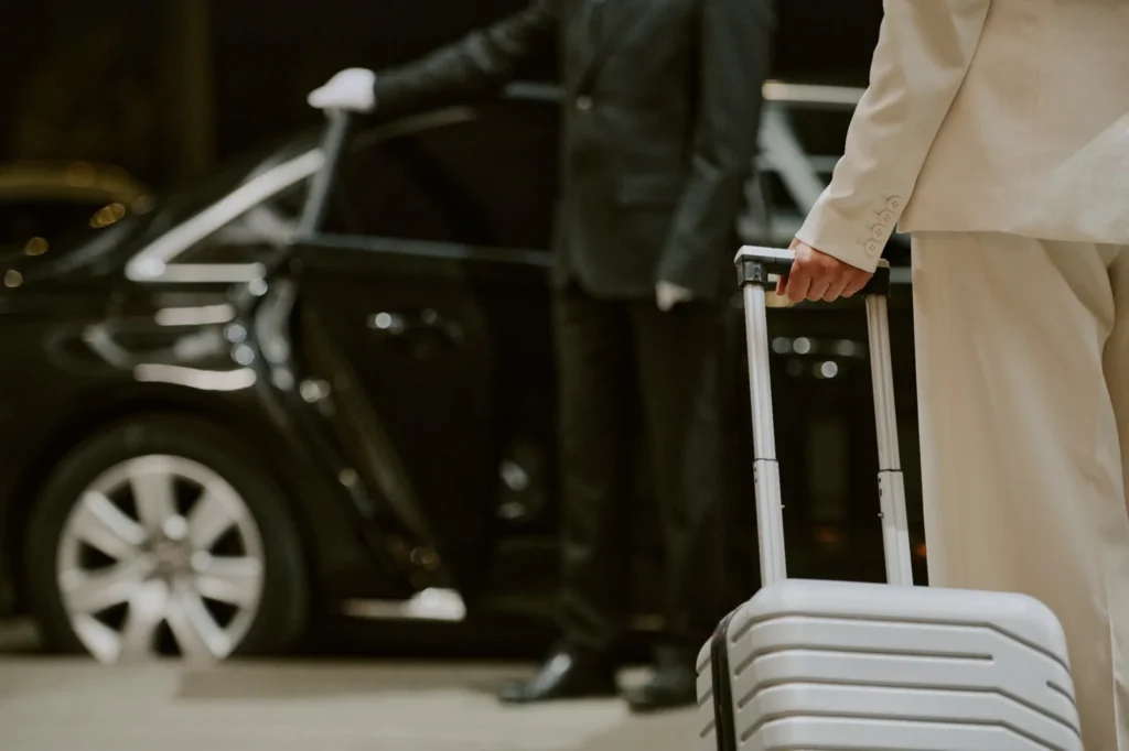 A traveller with luggage beside a waiting vehicle.