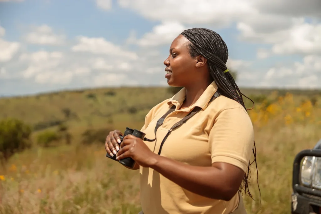 A guide holding binoculars beside a safari vehicle.