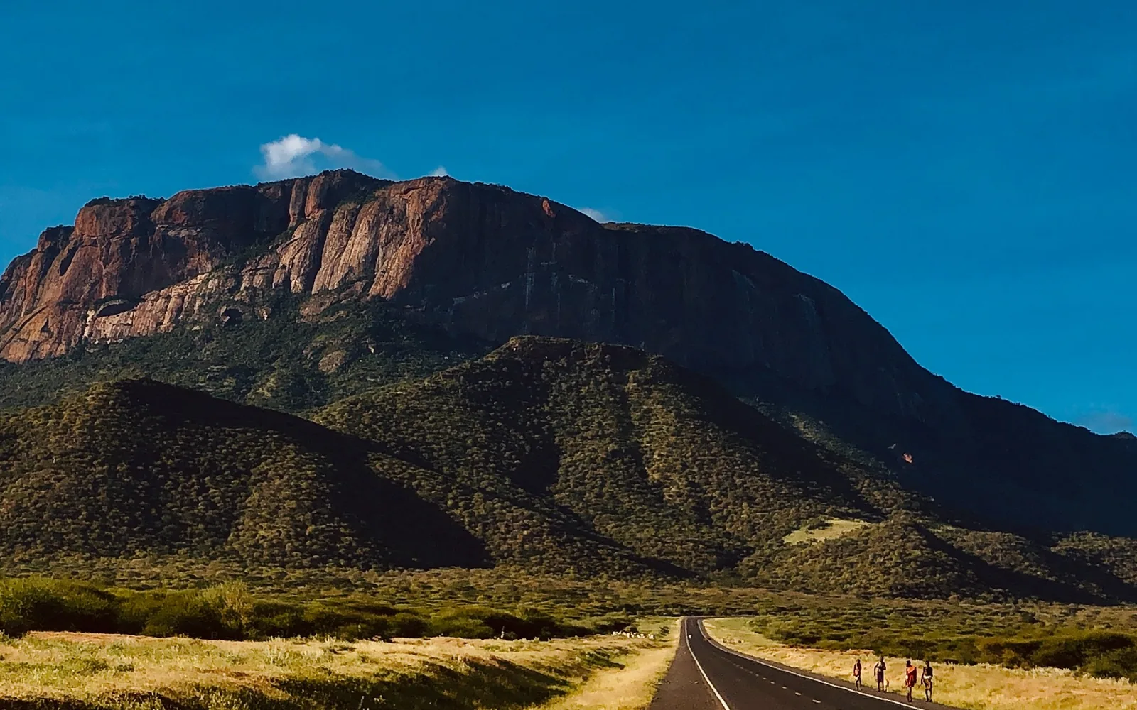 A paved road leading towards a broad rocky escarpment.