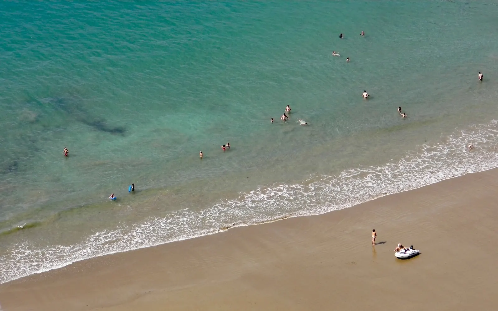An aerial view of turquoise water meeting a sandy shore.