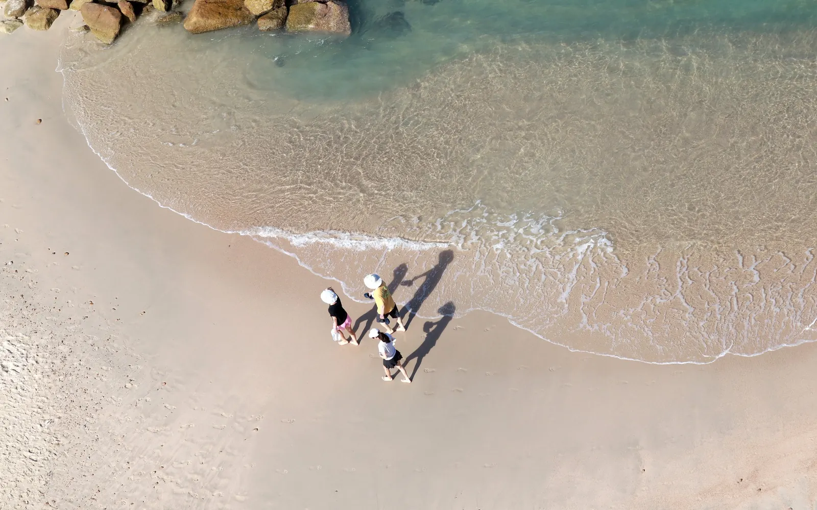An overhead view of people walking beside clear coastal water.