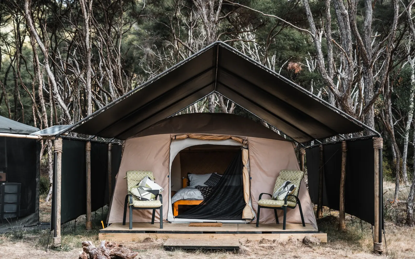 A canvas tent with a covered sitting area among trees.