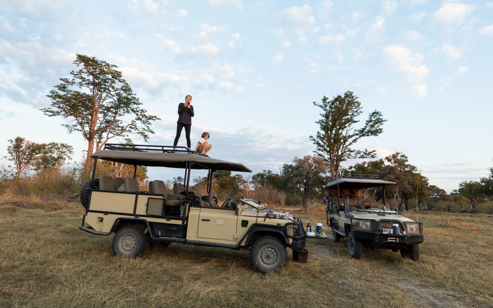 Travellers pausing beside safari vehicles in an open landscape.
